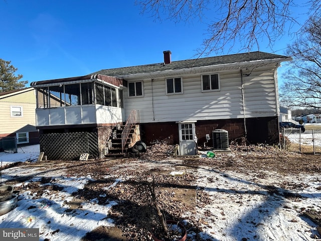 snow covered rear of property featuring cooling unit and a sunroom