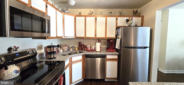 kitchen with appliances with stainless steel finishes, dark hardwood / wood-style floors, white cabinetry, sink, and light stone countertops