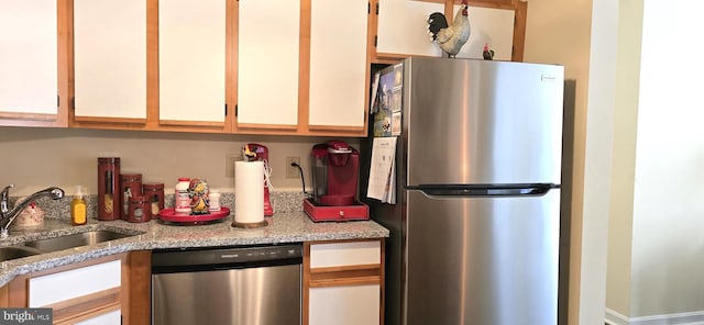 kitchen featuring stainless steel appliances, light stone countertops, sink, and white cabinets