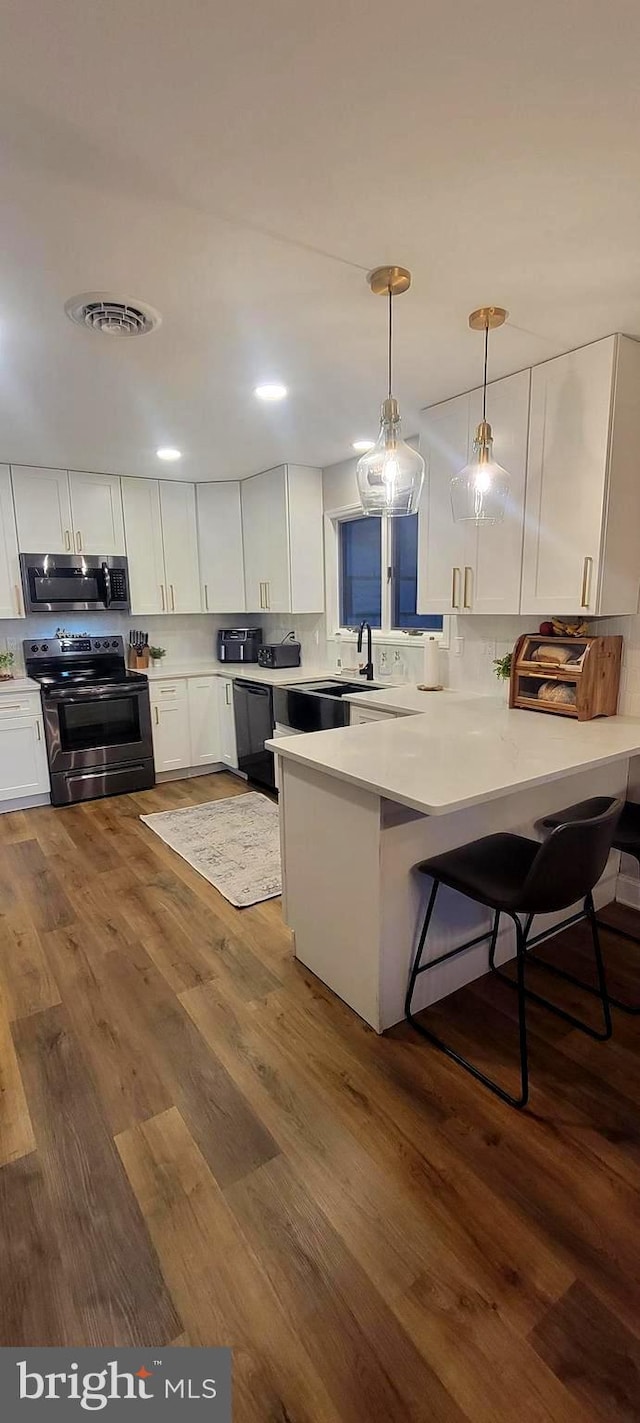 kitchen featuring hanging light fixtures, dark hardwood / wood-style floors, kitchen peninsula, stainless steel appliances, and white cabinets