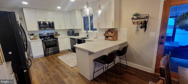 kitchen featuring a kitchen breakfast bar, black appliances, white cabinets, decorative light fixtures, and kitchen peninsula