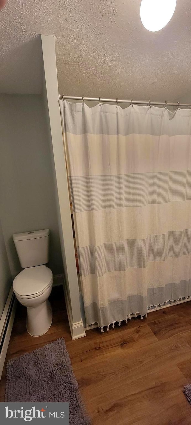 bathroom featuring a textured ceiling, wood-type flooring, a baseboard radiator, and toilet