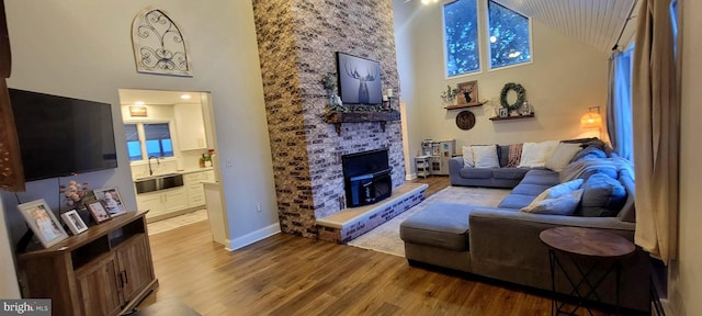 living room featuring a towering ceiling, a large fireplace, sink, and light wood-type flooring