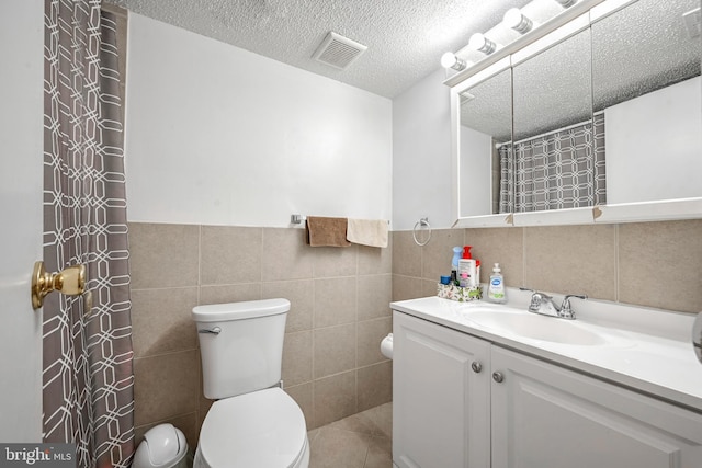 bathroom with toilet, tile walls, a textured ceiling, vanity, and tile patterned flooring