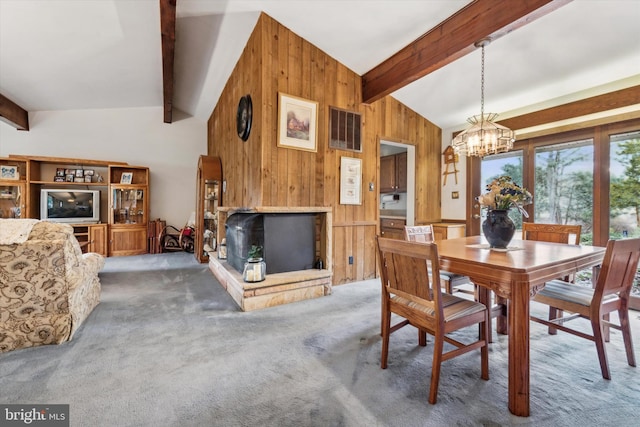 carpeted dining area featuring vaulted ceiling with beams, a chandelier, and wood walls