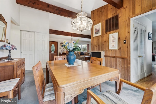 dining room featuring beam ceiling, dark colored carpet, a chandelier, and wood walls