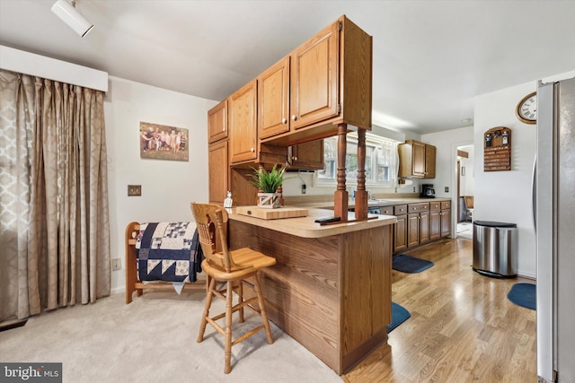 kitchen with stainless steel refrigerator, a kitchen breakfast bar, kitchen peninsula, and light wood-type flooring