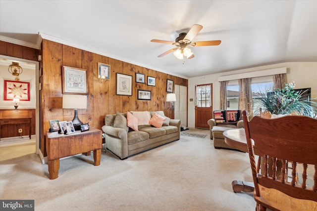 carpeted living room with ceiling fan, ornamental molding, and wooden walls