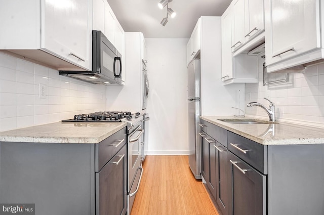 kitchen with sink, white cabinets, light hardwood / wood-style floors, stainless steel appliances, and light stone countertops