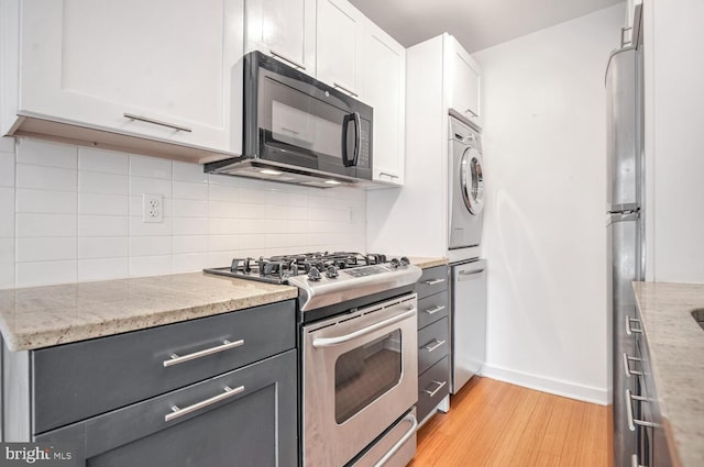 kitchen featuring white cabinetry, decorative backsplash, stacked washer / dryer, and appliances with stainless steel finishes