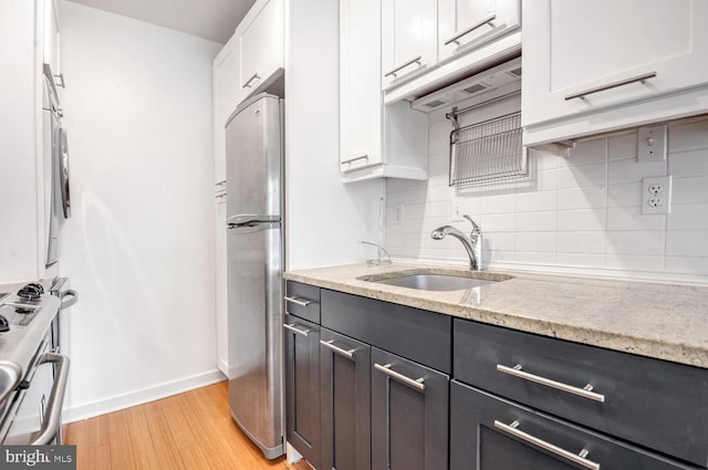 kitchen featuring sink, white cabinetry, stainless steel appliances, light stone countertops, and light wood-type flooring