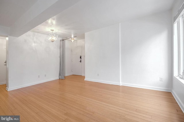 spare room featuring plenty of natural light, an inviting chandelier, and light wood-type flooring