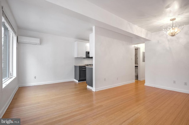 unfurnished living room with plenty of natural light, a chandelier, a wall mounted air conditioner, and light wood-type flooring