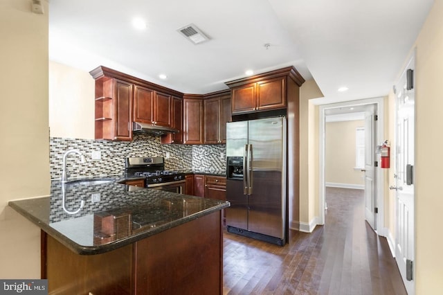 kitchen with sink, dark wood-type flooring, dark stone countertops, stainless steel appliances, and kitchen peninsula