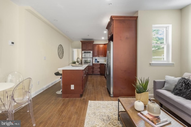 kitchen with dark wood-type flooring, stainless steel appliances, an island with sink, and a breakfast bar area