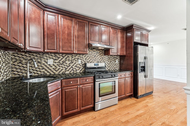 kitchen with appliances with stainless steel finishes, sink, decorative backsplash, dark stone counters, and light hardwood / wood-style floors