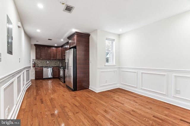 kitchen with dark brown cabinetry, light wood-type flooring, appliances with stainless steel finishes, electric panel, and decorative backsplash