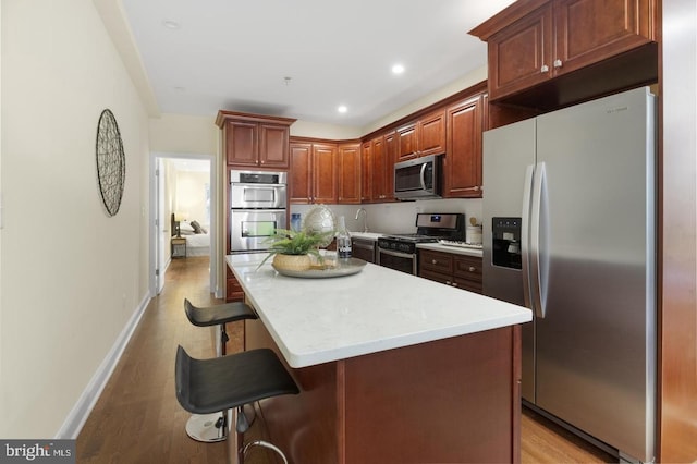 kitchen with stainless steel appliances, a kitchen island, a breakfast bar area, and light hardwood / wood-style floors