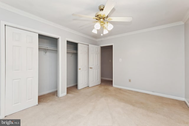 unfurnished bedroom featuring multiple closets, ornamental molding, light colored carpet, and ceiling fan