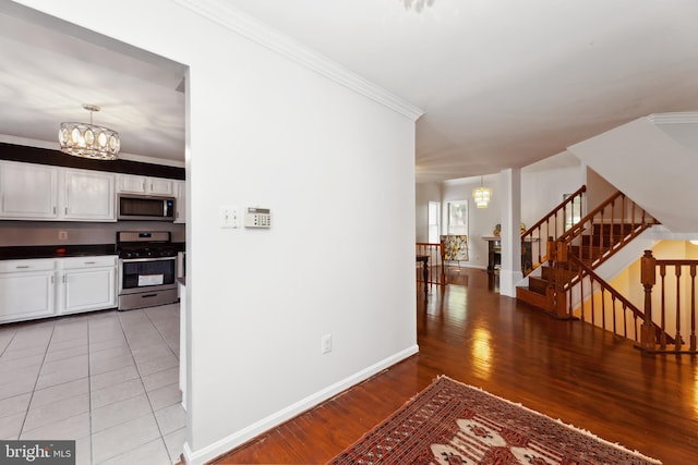 interior space with appliances with stainless steel finishes, white cabinets, hanging light fixtures, crown molding, and an inviting chandelier