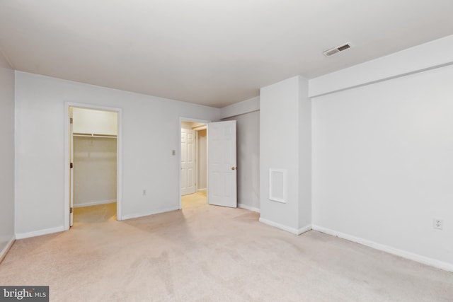 unfurnished bedroom with a walk in closet, light colored carpet, and a closet