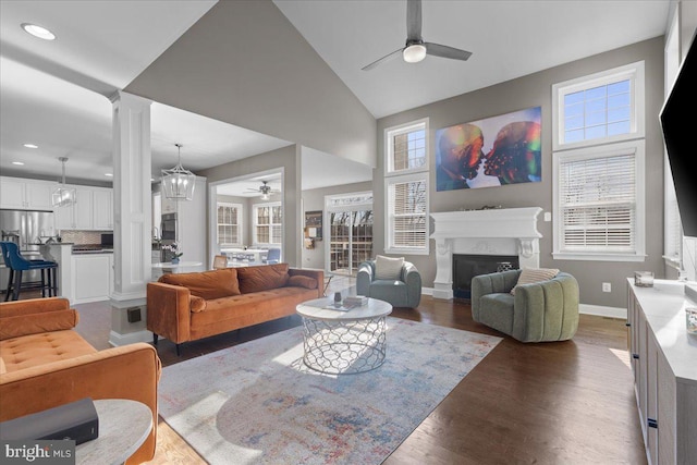 living room featuring ceiling fan with notable chandelier, high vaulted ceiling, dark wood-type flooring, and decorative columns