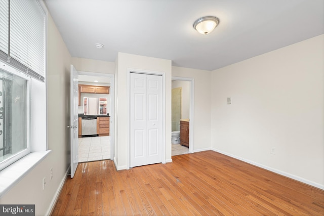 unfurnished bedroom with light wood-type flooring, multiple windows, baseboards, and a closet