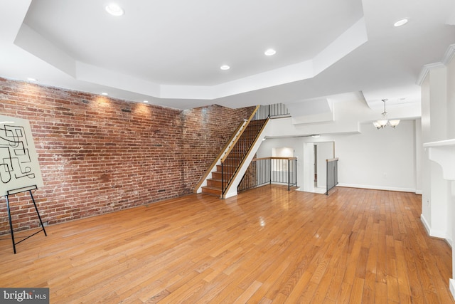 unfurnished living room with brick wall, baseboards, stairway, a tray ceiling, and wood-type flooring