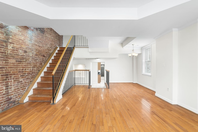 unfurnished living room with light wood-style floors, a chandelier, baseboards, and brick wall