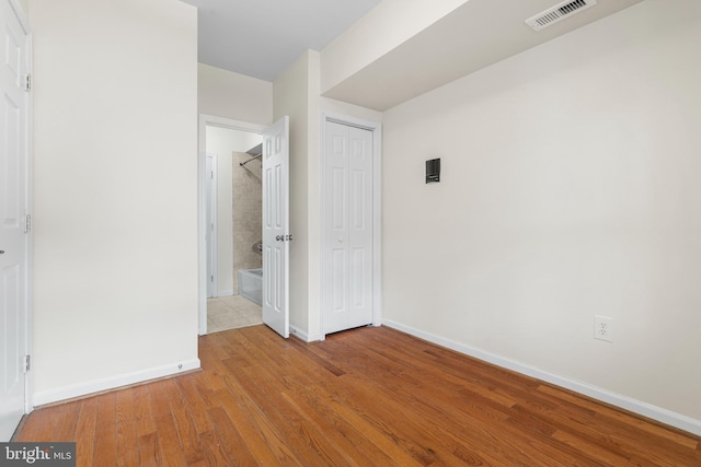 unfurnished bedroom with ensuite bathroom, wood finished floors, visible vents, baseboards, and a closet