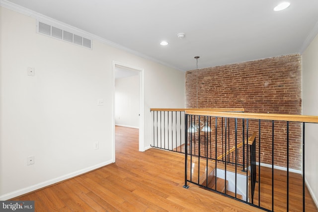 hallway with baseboards, visible vents, brick wall, ornamental molding, and wood finished floors