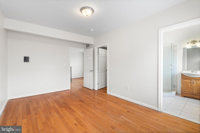 unfurnished bedroom featuring light wood finished floors, ensuite bath, a sink, and baseboards