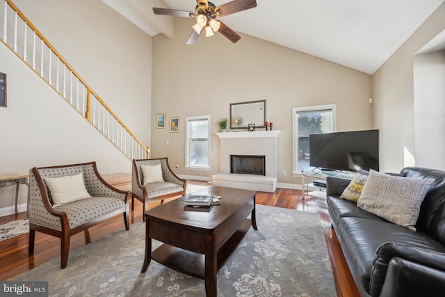 living room featuring a fireplace, wood-type flooring, high vaulted ceiling, and ceiling fan