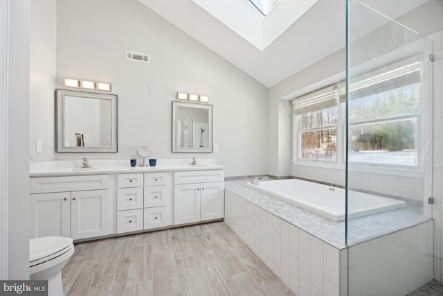 bathroom featuring hardwood / wood-style flooring, vanity, vaulted ceiling with skylight, and tiled tub