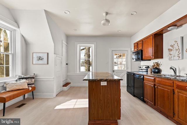 kitchen featuring dark stone countertops, light wood-type flooring, a kitchen island, and black appliances