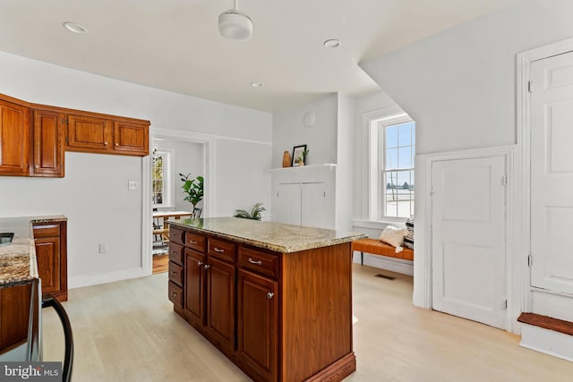 kitchen with light stone counters, a center island, and light wood-type flooring