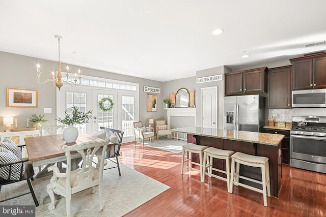 kitchen featuring a breakfast bar area, appliances with stainless steel finishes, a center island, light stone counters, and dark brown cabinetry