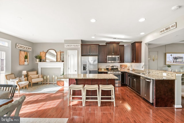 kitchen featuring dark wood-type flooring, a kitchen bar, sink, appliances with stainless steel finishes, and light stone countertops