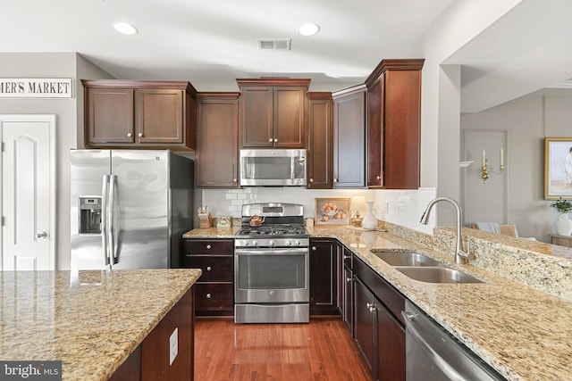 kitchen with stainless steel appliances, dark hardwood / wood-style flooring, light stone countertops, and sink