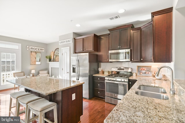 kitchen with sink, dark wood-type flooring, appliances with stainless steel finishes, light stone countertops, and a kitchen bar