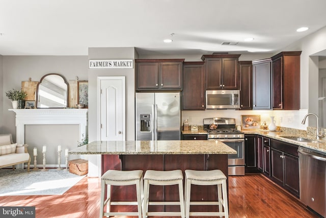 kitchen with appliances with stainless steel finishes, a breakfast bar, sink, a center island, and light stone countertops