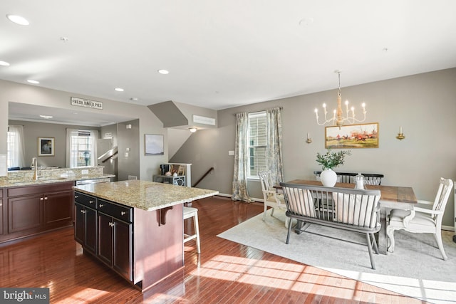 kitchen with a kitchen bar, sink, decorative light fixtures, a kitchen island, and light stone countertops