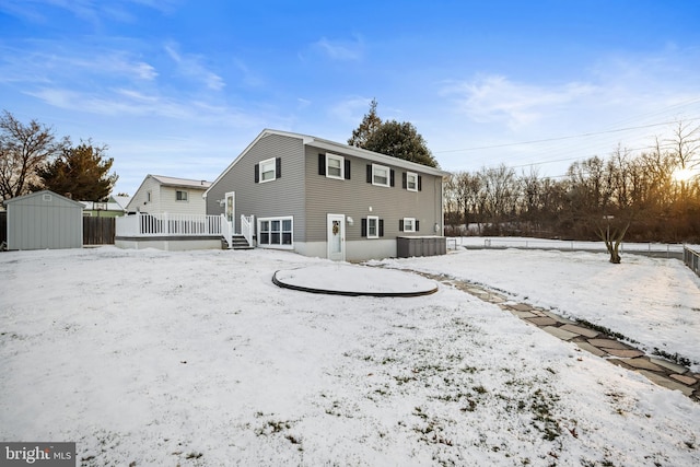 snow covered house with a wooden deck and a storage unit