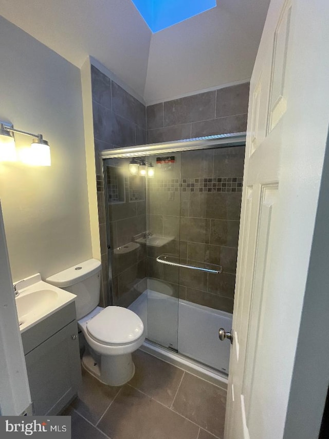 bathroom with a skylight, a shower with shower door, vanity, toilet, and tile patterned floors