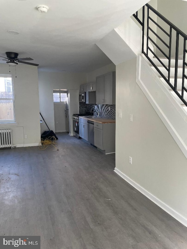 unfurnished living room with dark hardwood / wood-style floors, radiator heating unit, and ceiling fan