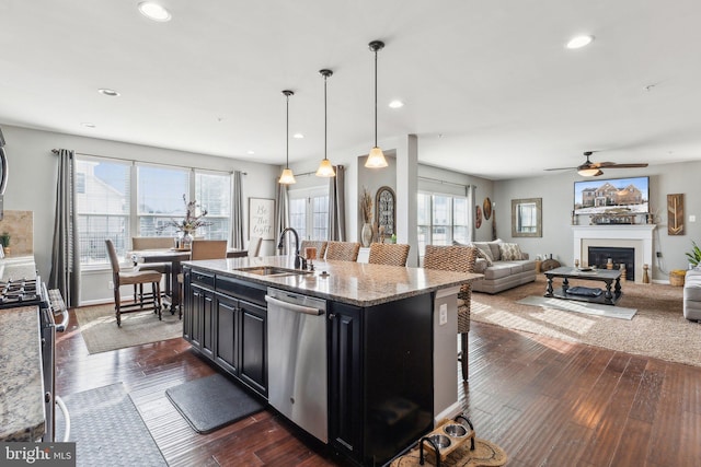 kitchen featuring a kitchen bar, sink, an island with sink, stainless steel appliances, and light stone countertops