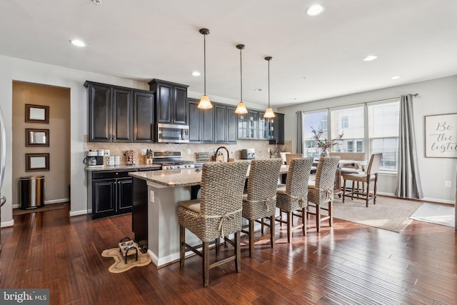 kitchen with appliances with stainless steel finishes, dark hardwood / wood-style floors, pendant lighting, a kitchen bar, and a kitchen island with sink