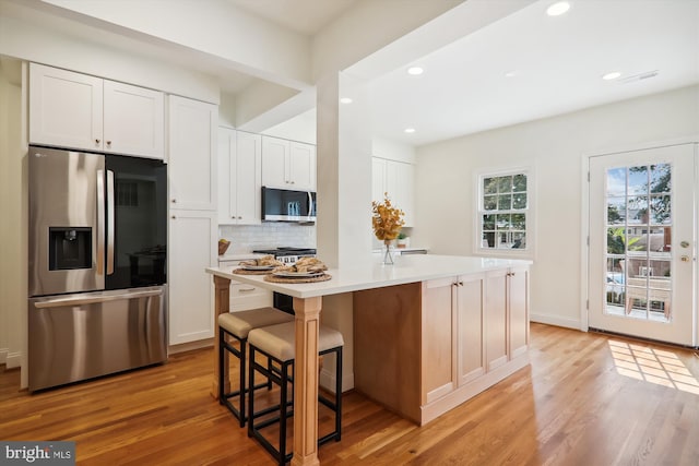 kitchen featuring white cabinetry, stainless steel appliances, a kitchen island, and light wood-type flooring