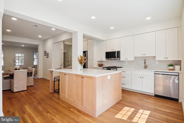 kitchen with sink, white cabinetry, stainless steel appliances, a kitchen island, and light wood-type flooring