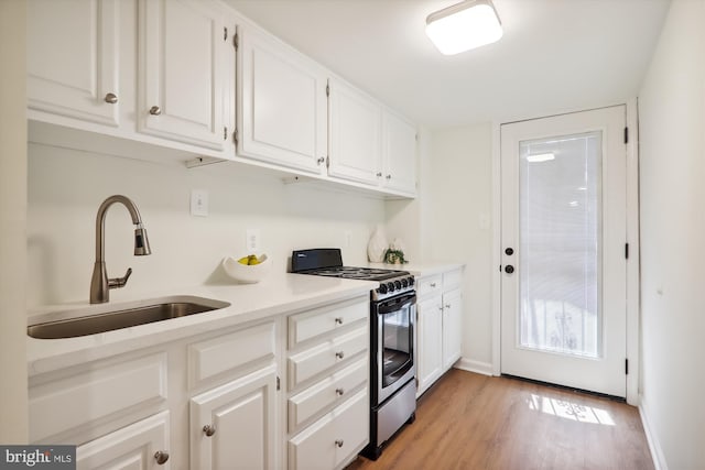 kitchen with sink, light hardwood / wood-style floors, stainless steel range with gas stovetop, and white cabinets